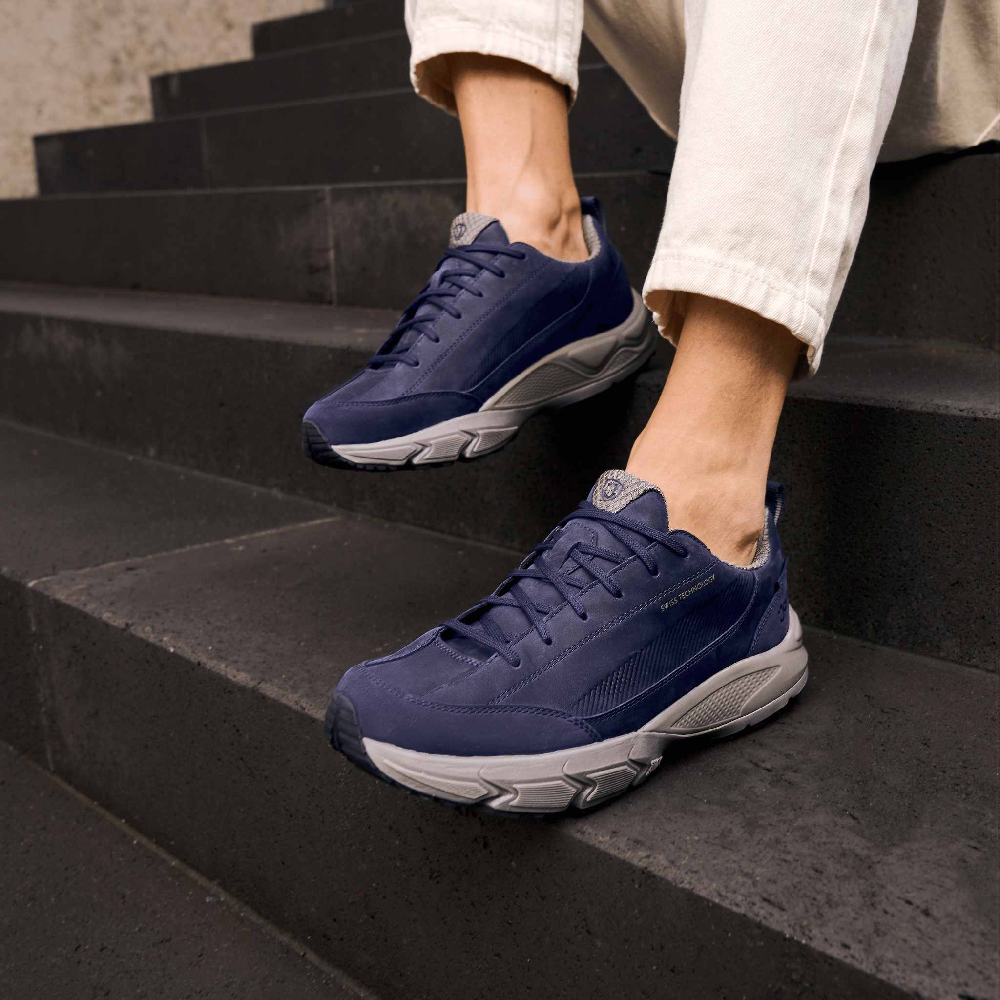 A person wearing navy blue Skechers sneakers with white and gray soles, sitting on dark outdoor steps.