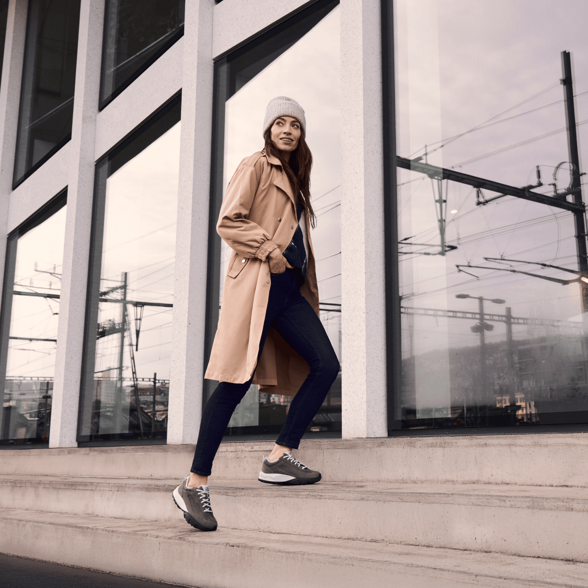 women walking up stairs in a beige coat and black pants wearing dark grey joya sneakers