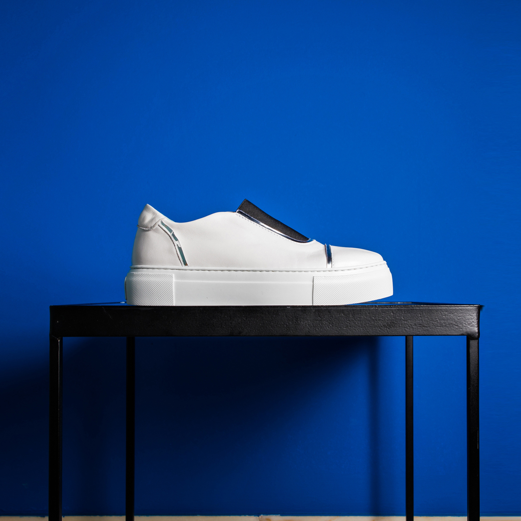 White sneaker with black sole on a black table against a blue background