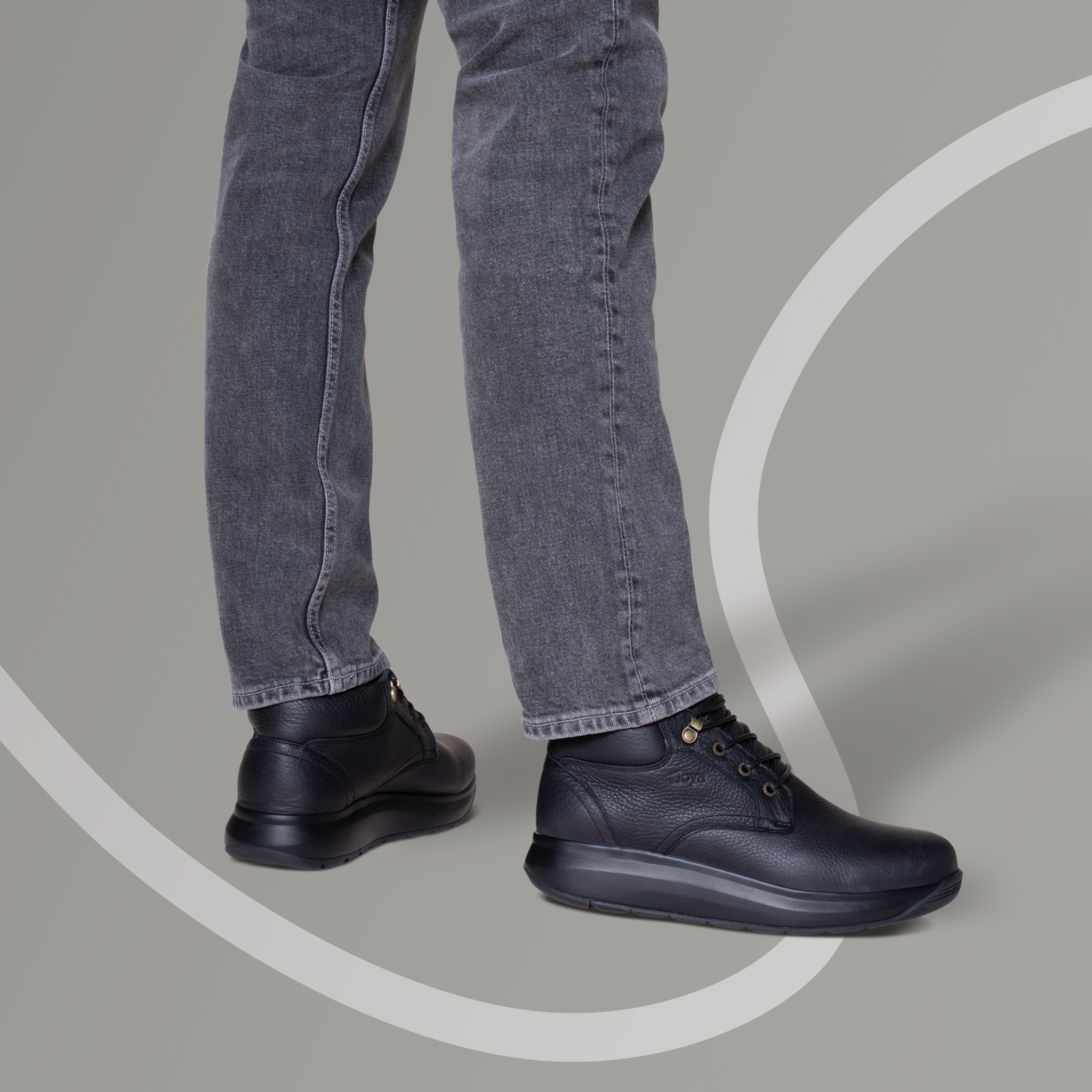 Black shoes worn with gray jeans on a gray background