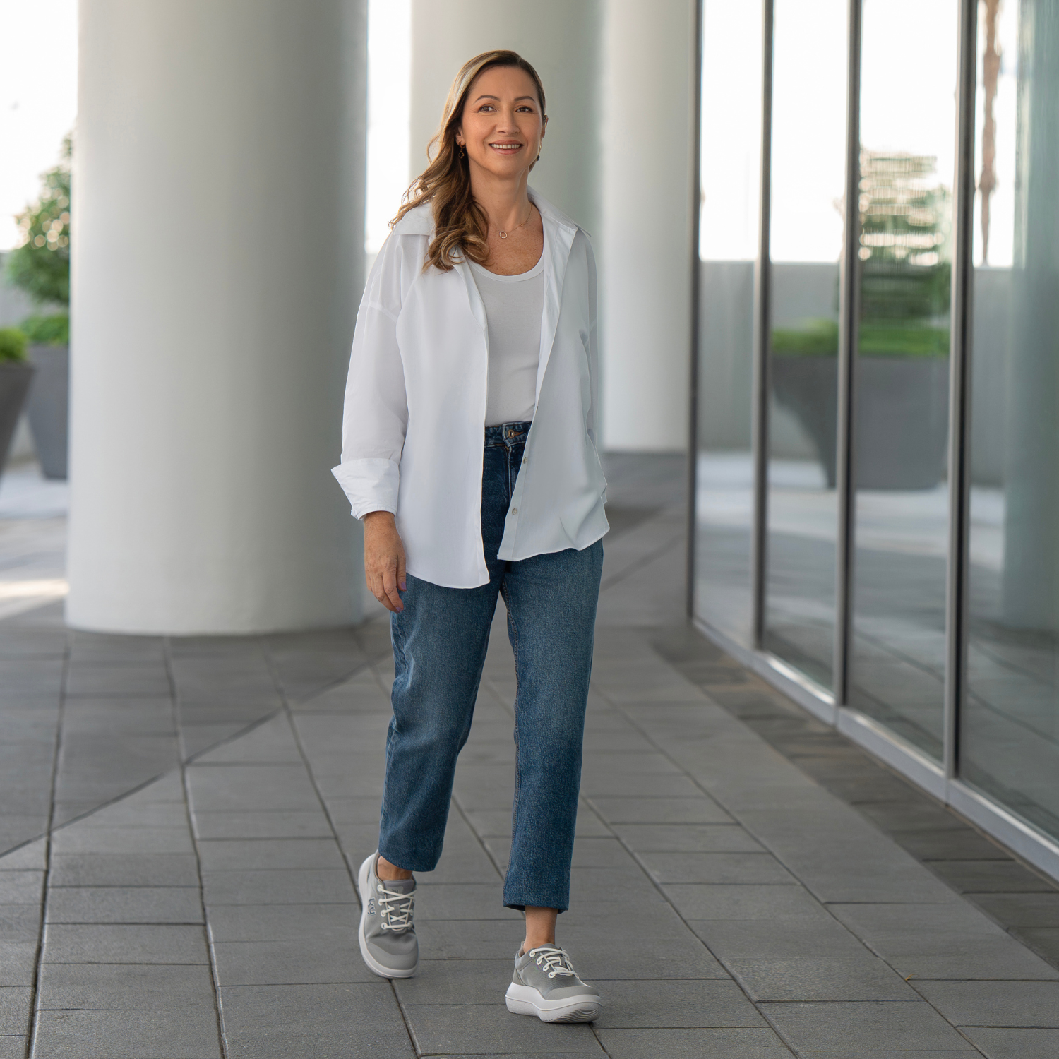 Woman in white shirt and blue jeans standing in front of a modern building.