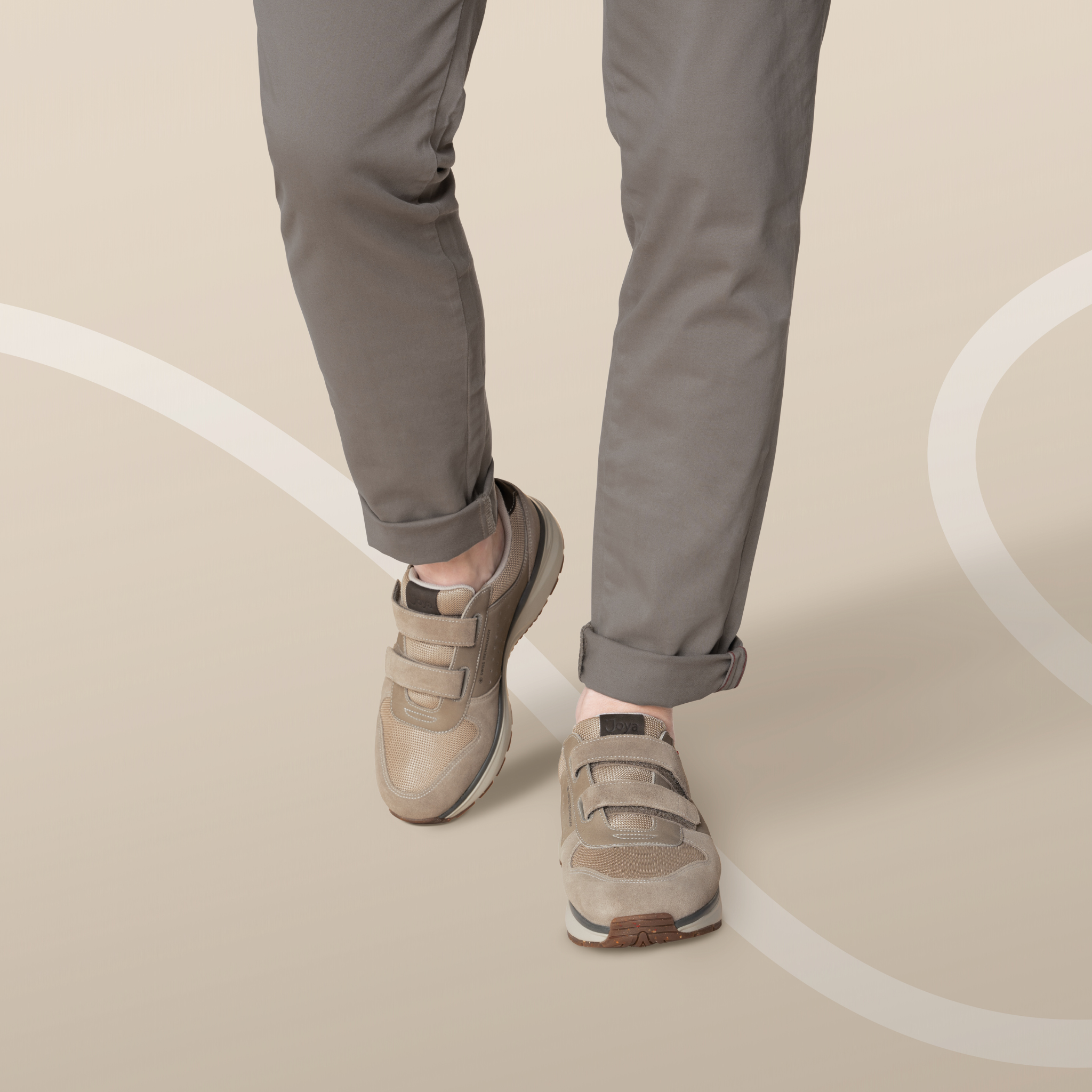 Person wearing beige sneakers and gray pants on a beige background