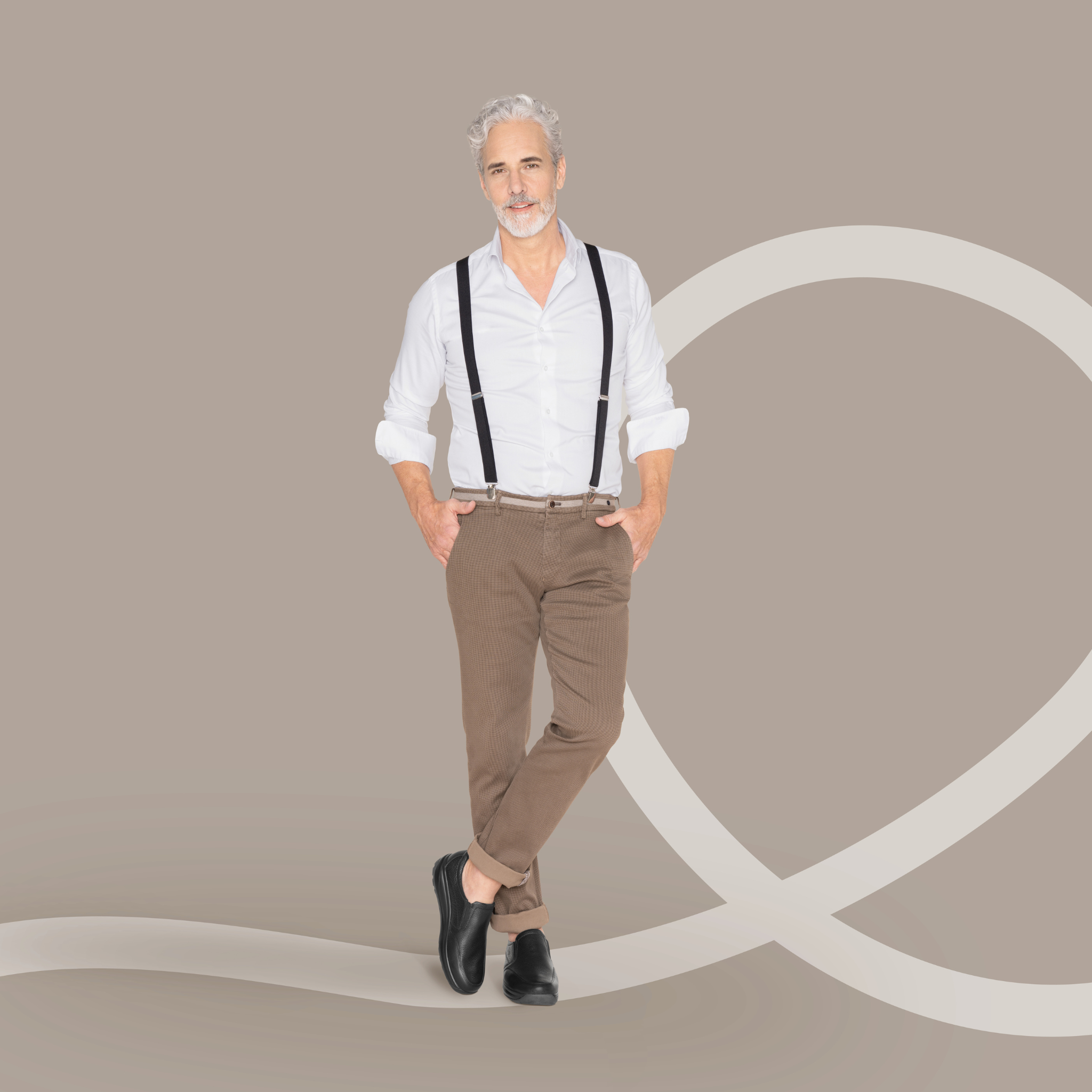 Man wearing a white shirt, brown pants, and suspenders against a beige background
