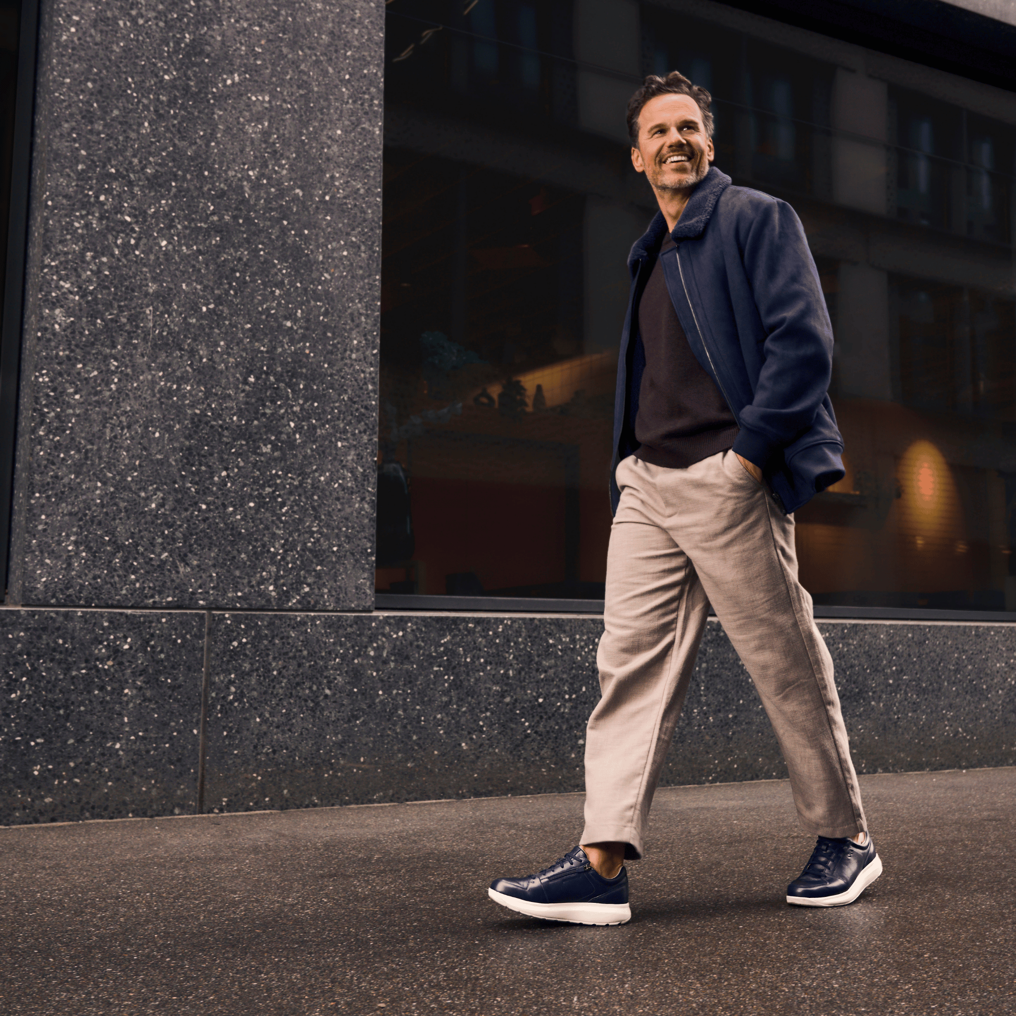 man walking wearing dark blue sneakers with white soles with a building in the background