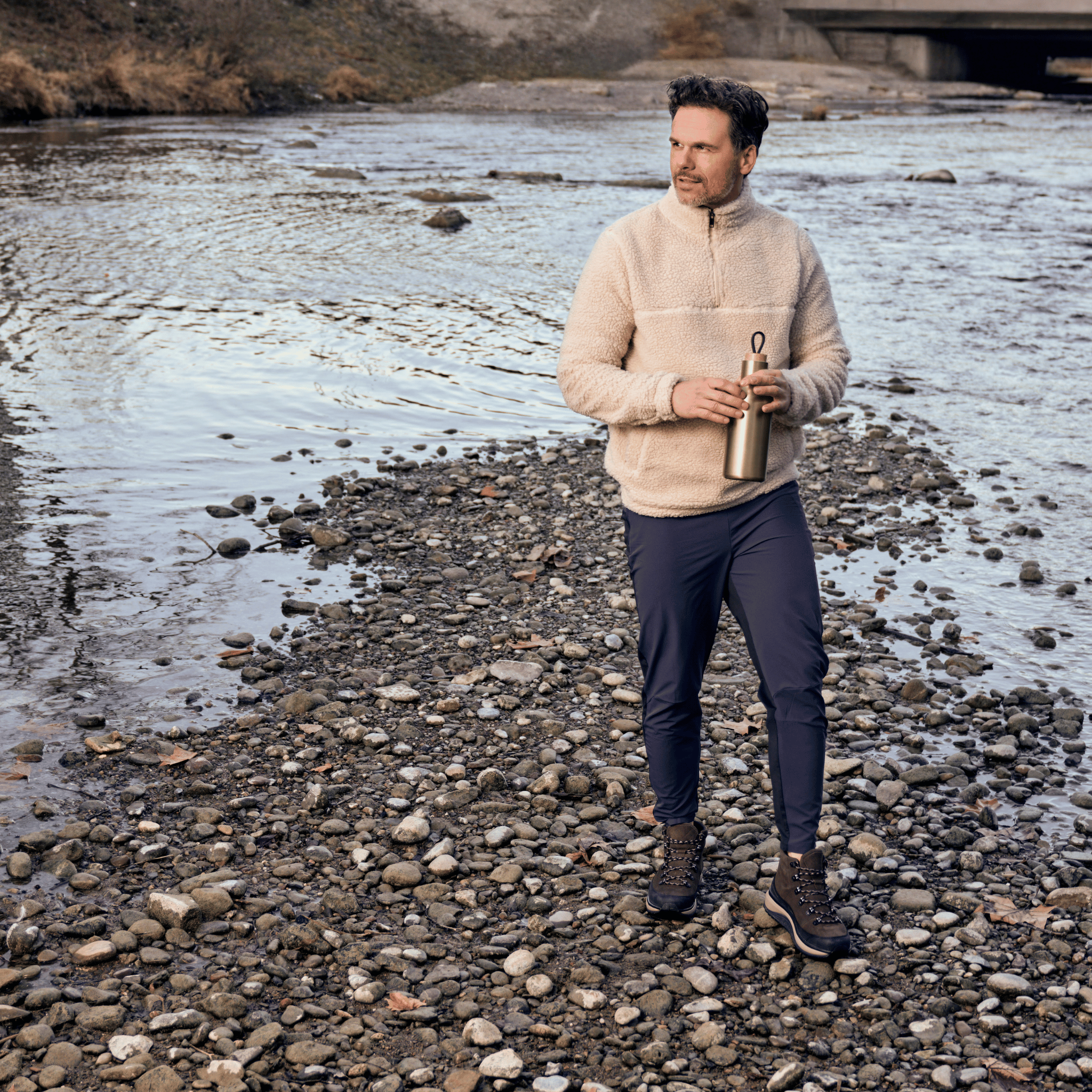 man standing on river bed with rocks wearing brown boots