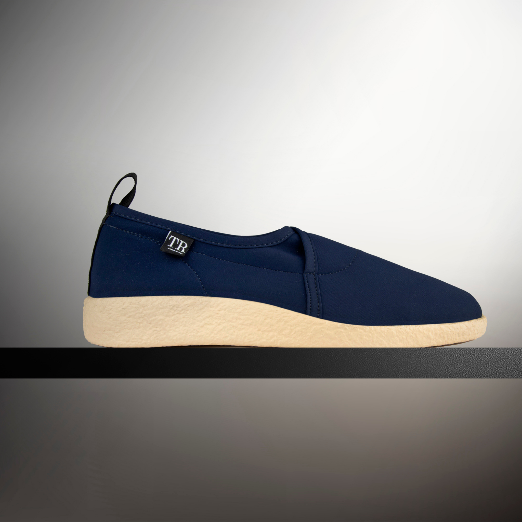 Navy slip-on shoe with beige sole on a gradient gray background