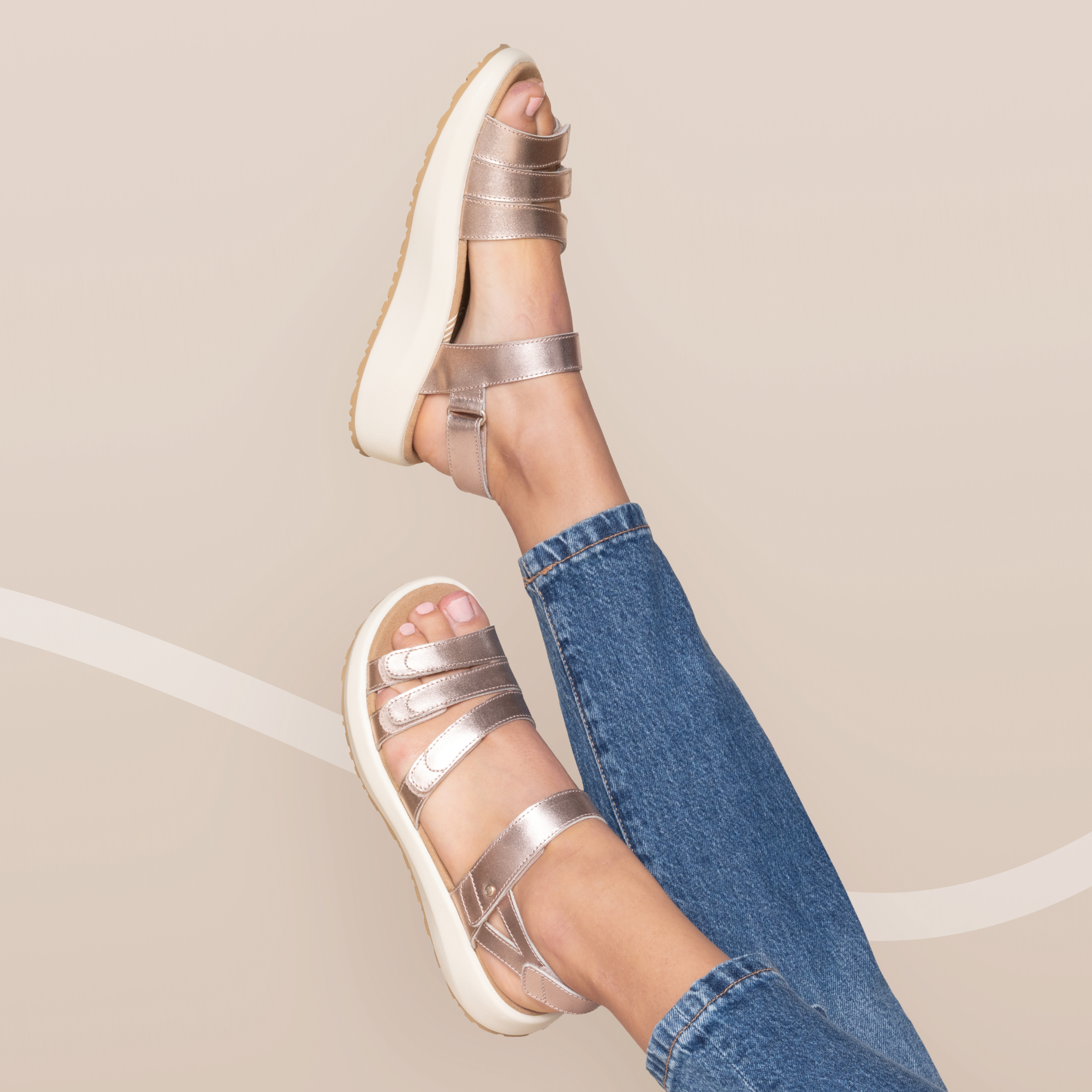 Silver sandals worn with blue jeans on a neutral background