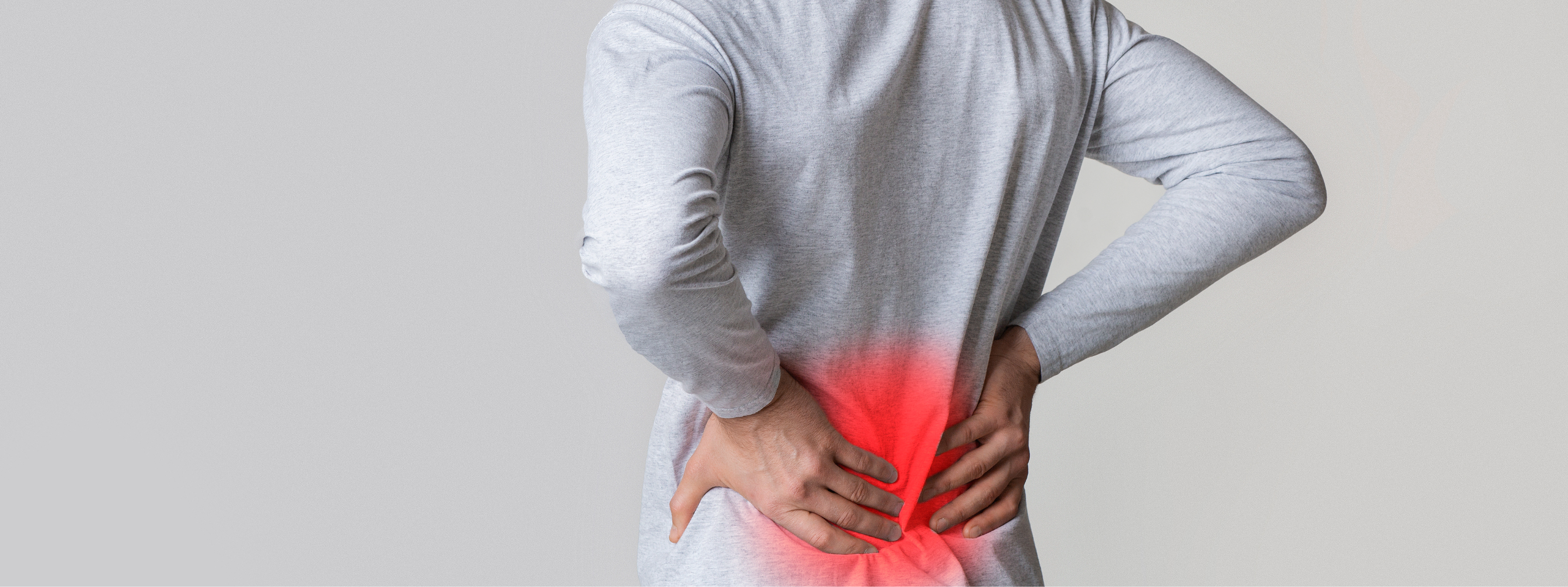A person from the back wearing a light gray long-sleeve shirt, holding their lower back with both hands. A red glow effect highlights the lower back area, set against a solid light gray background.
