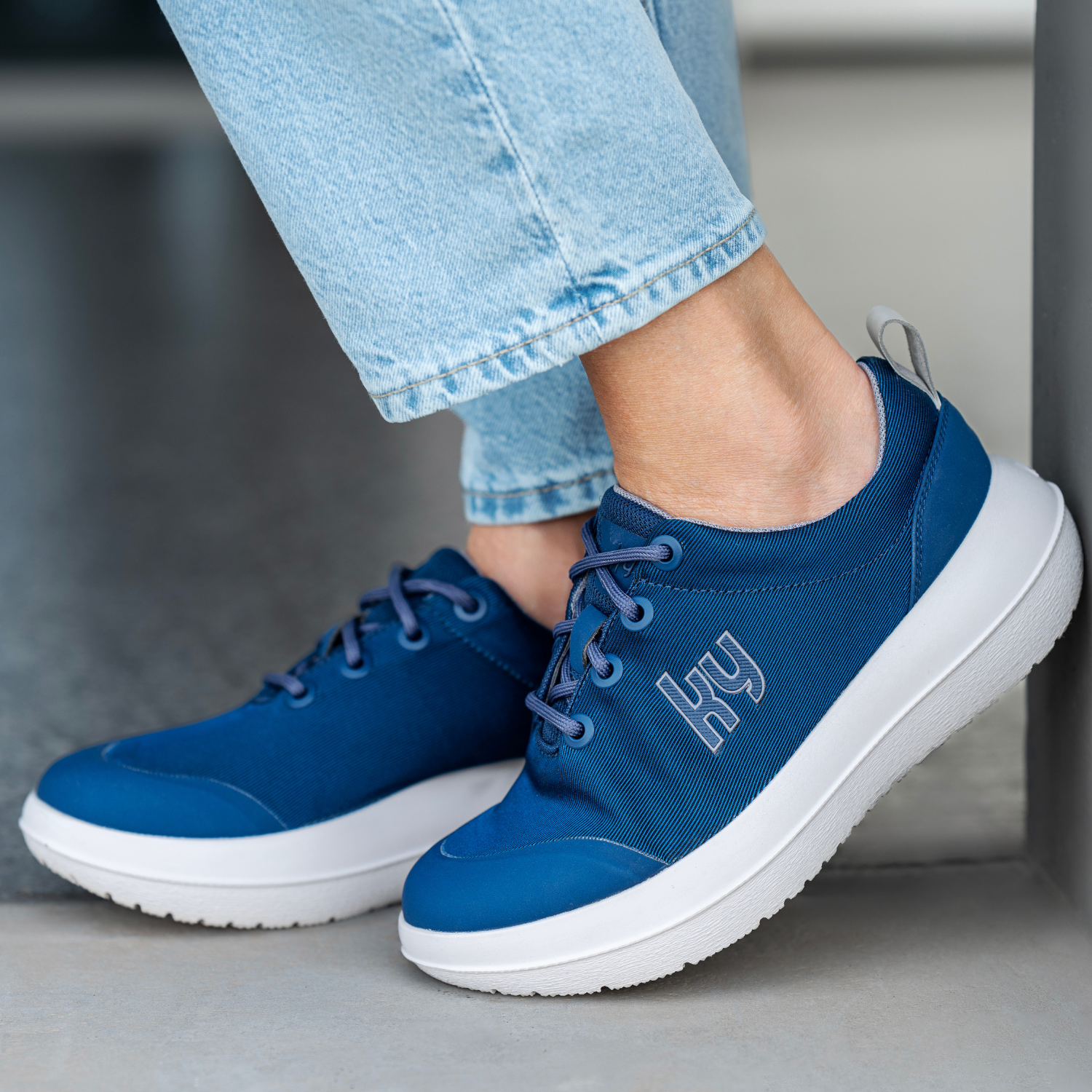 Blue sneakers with white soles worn with light blue jeans on a neutral background